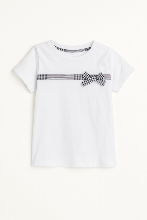 Remera infantil blanca de jersey con moño cuadrillé negro y blanco en el pecho