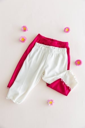 Dos calzas ciclistas infantiles de tela morley, color blanco y color fucsia magenta, mostrando el detalle del ruedo con terminación ruloté.