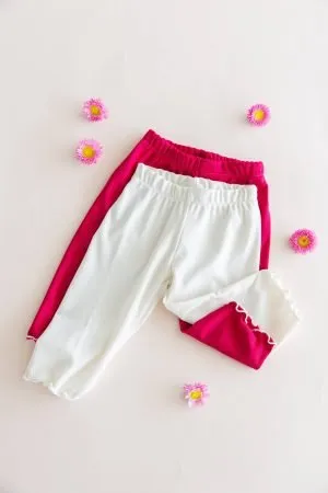 Dos calzas ciclistas infantiles de tela morley, color blanco y color fucsia magenta, mostrando el detalle del ruedo con terminación ruloté.