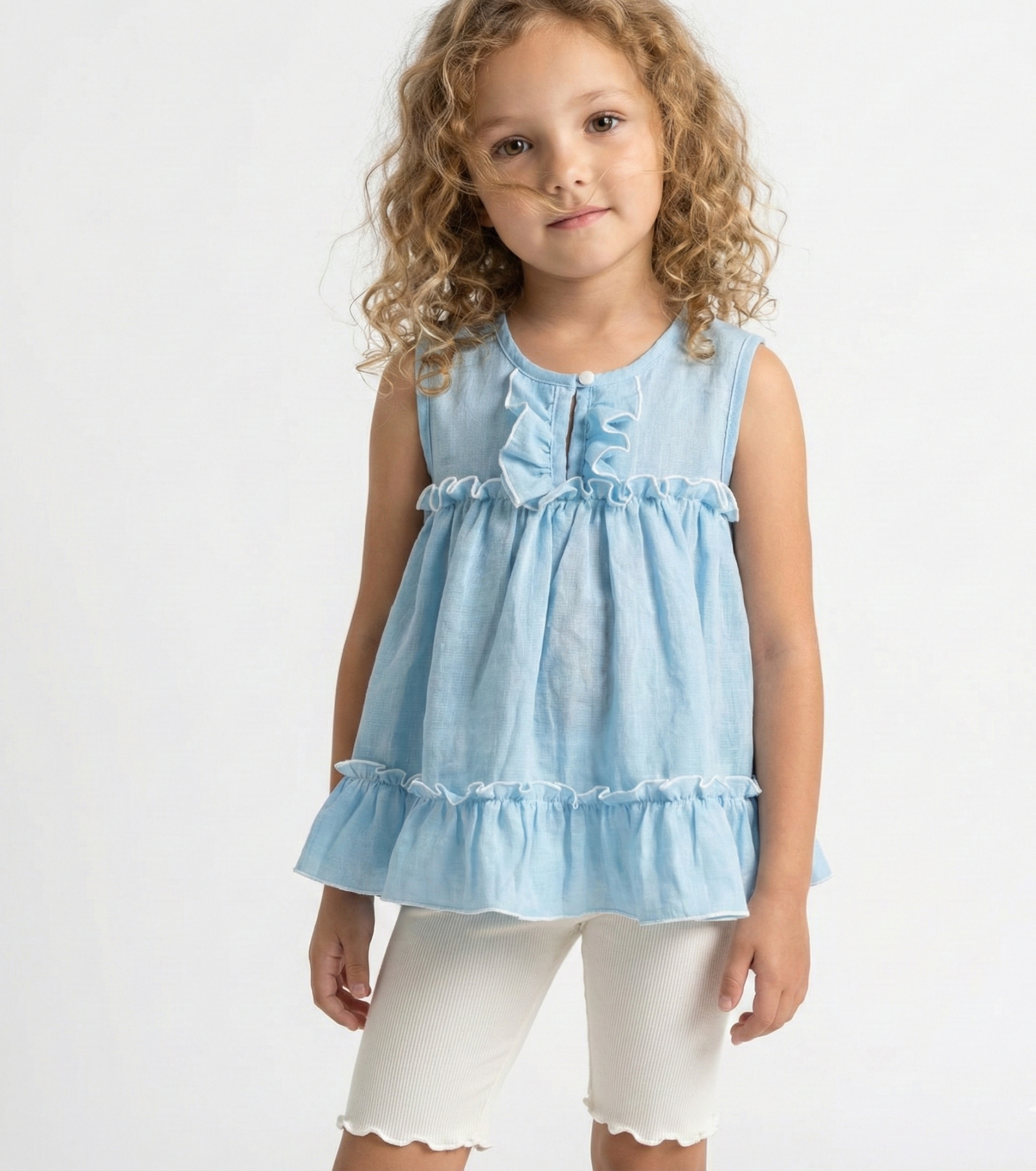Niña con cabello rizado usando una blusa celeste sin mangas de tela gasa tipo lino, con volados y bordes blancos festoneados. Ropa de verano elegante para niñas.