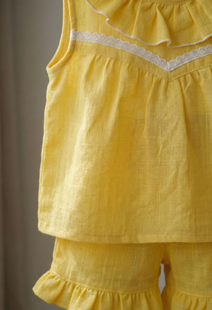 Primer plano de la tela del conjunto amarillo, mostrando la textura arrugada característica del lino coreano y el detalle de la puntilla blanca de algodón en el borde.
